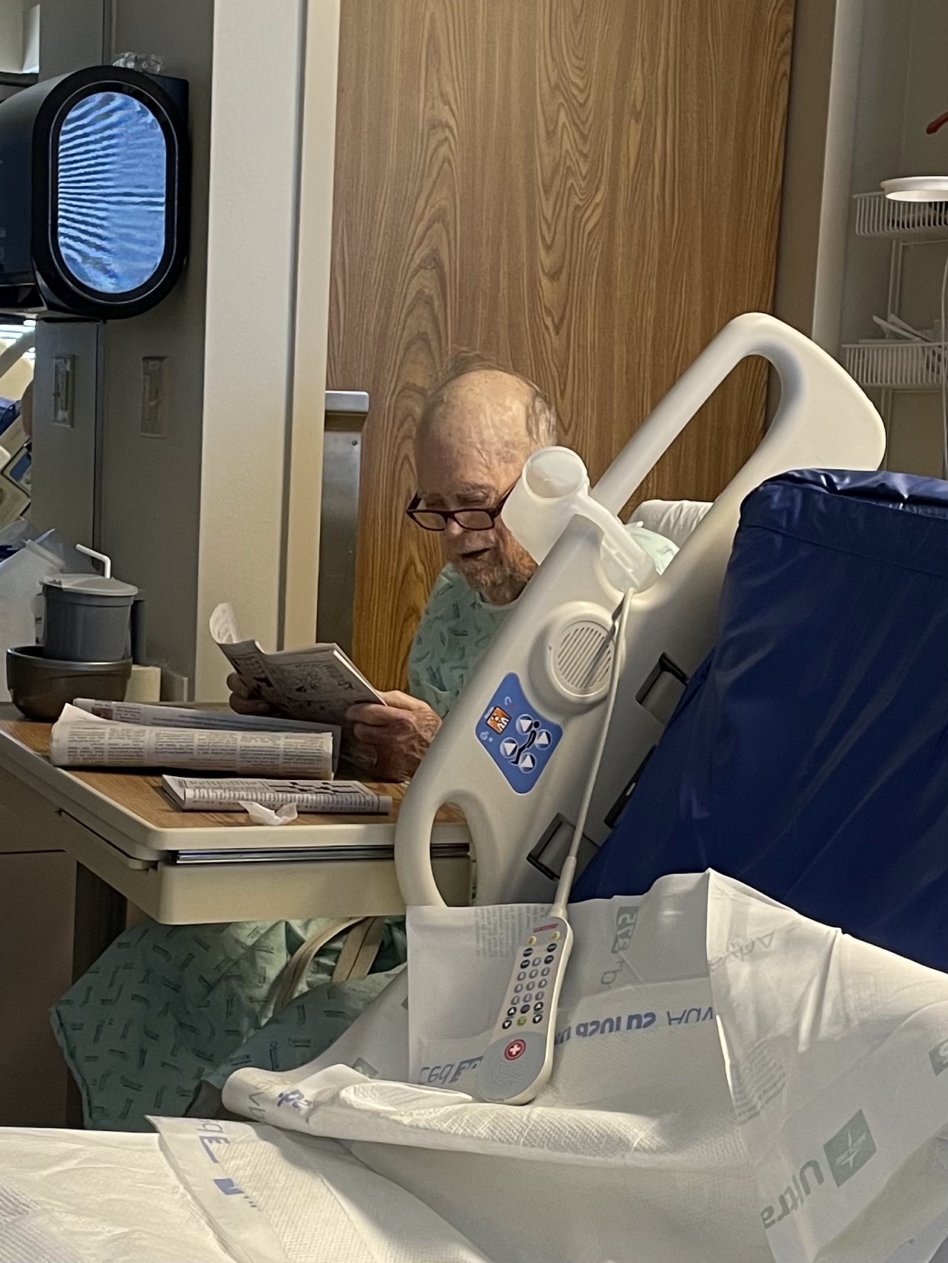 Dad sitting up in the hospital room reading the newspaper.
