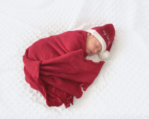 Newborn Lilly wrapped in a red blanket with a Christmas hat on.